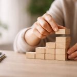 Mains empilant des blocs en bois formant un escalier progressif, symbolisant une reprise en main progressive et structurée.